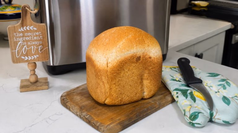 Homemade bread machine maple wheat bread with three slices on a wooden cutting board.