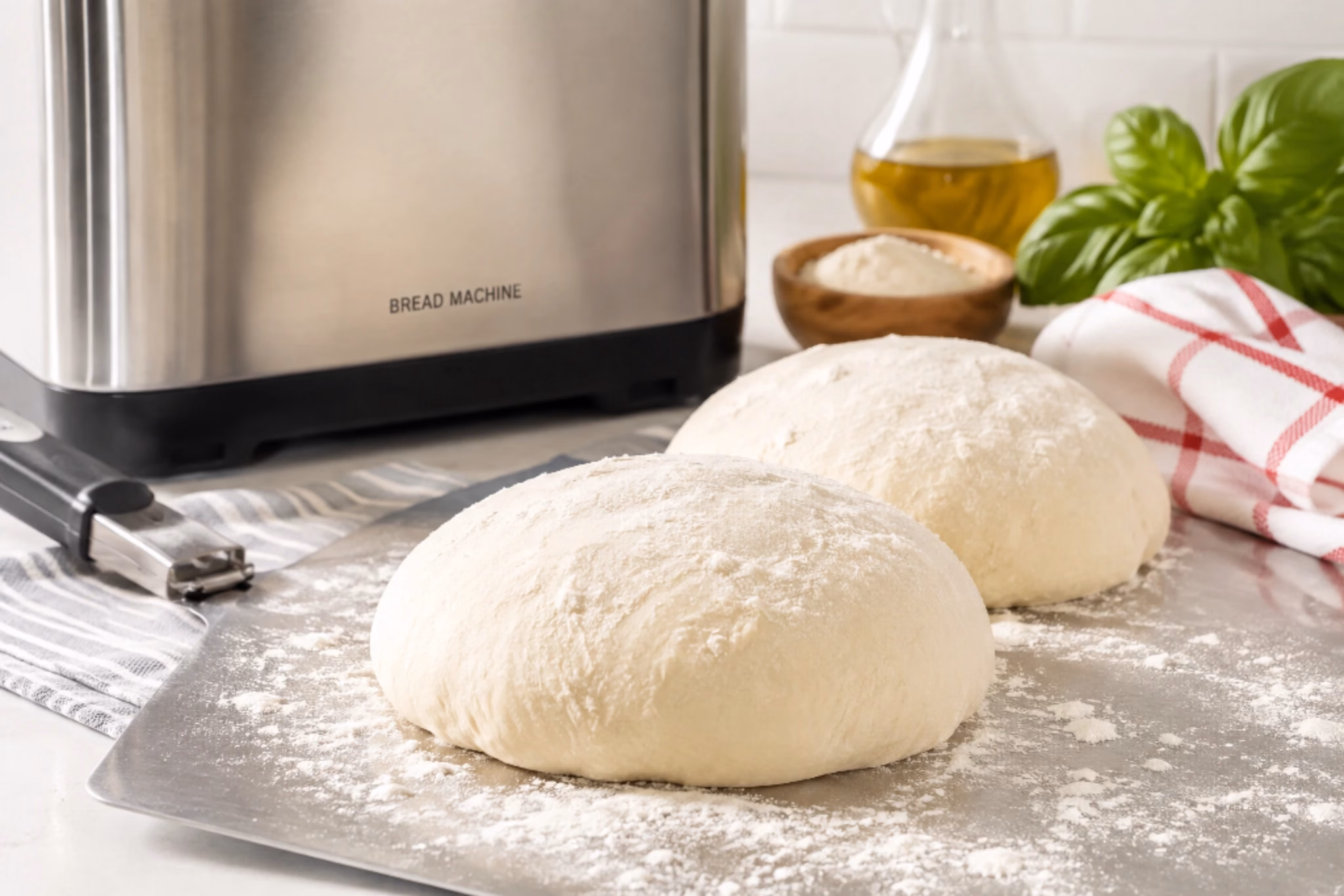 Two balls of homemade bread machine pizza dough on a floured surface with a bread machine in the background.