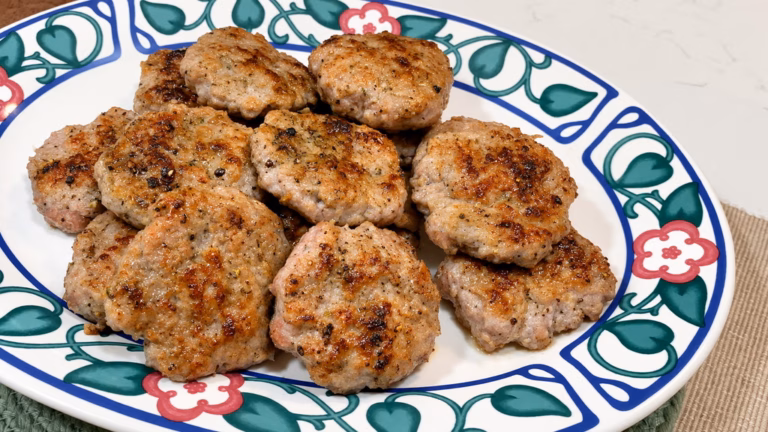 Homemade breakfast sausage patties with maple syrup, fennel, herbs, and cracked black pepper in a skillet.